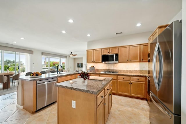 kitchen featuring sink, kitchen peninsula, a kitchen island, stainless steel appliances, and light stone countertops