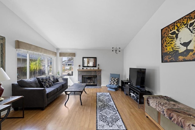 living room with a tiled fireplace, vaulted ceiling, and light wood-type flooring