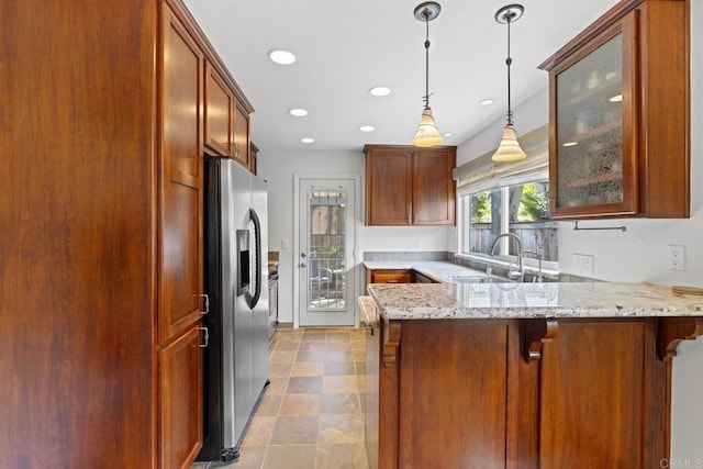 kitchen with decorative light fixtures, sink, stainless steel fridge, kitchen peninsula, and light stone countertops