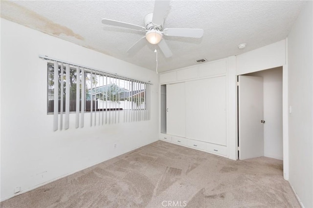 unfurnished bedroom with ceiling fan, light colored carpet, a textured ceiling, and a closet