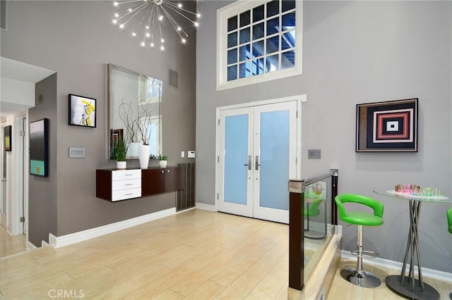 foyer with a high ceiling, light hardwood / wood-style floors, an inviting chandelier, and french doors