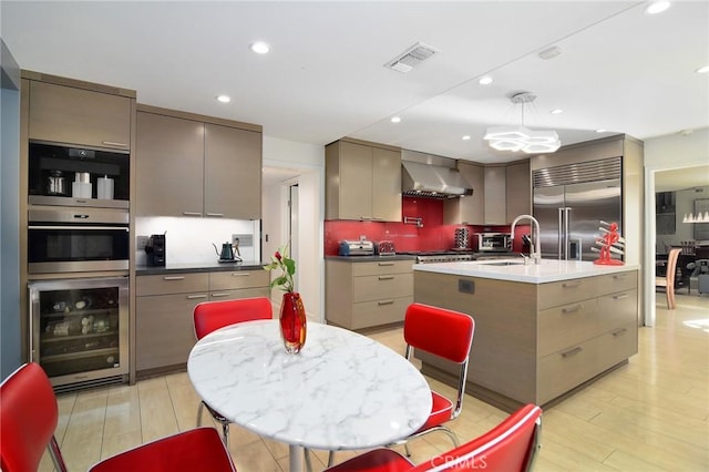 kitchen with wall chimney range hood, sink, appliances with stainless steel finishes, a kitchen island with sink, and beverage cooler