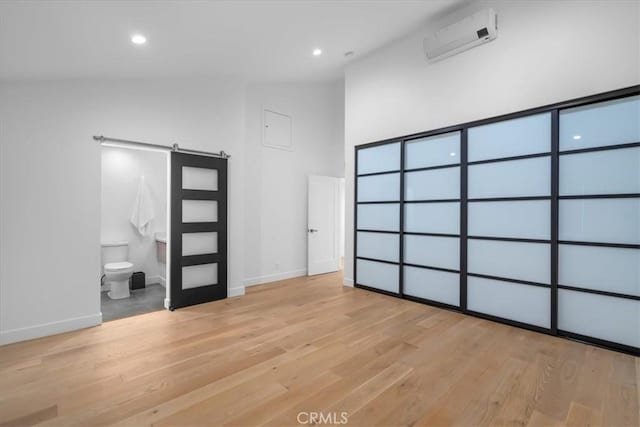 interior space featuring high vaulted ceiling, a barn door, a wall mounted air conditioner, and light wood-type flooring