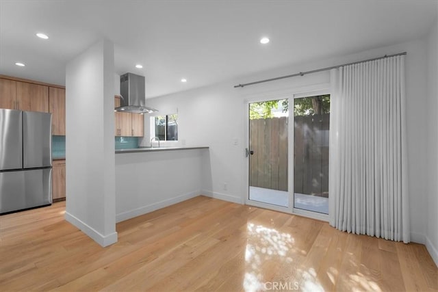 kitchen featuring sink, island range hood, light wood-type flooring, stainless steel fridge, and kitchen peninsula