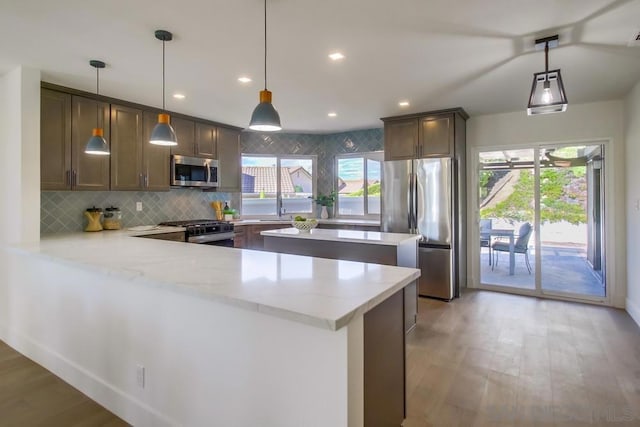 kitchen with pendant lighting, decorative backsplash, kitchen peninsula, stainless steel appliances, and light stone countertops