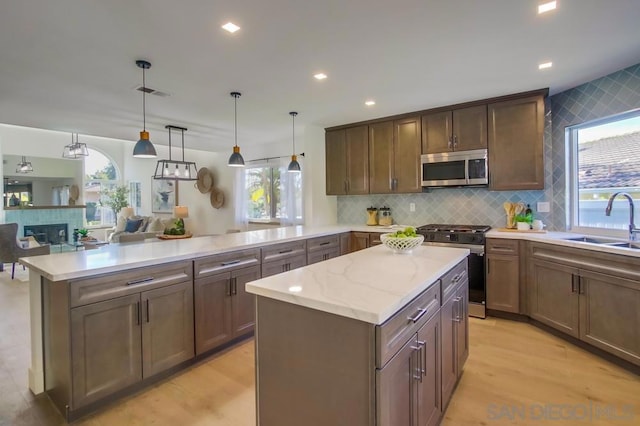 kitchen with pendant lighting, sink, appliances with stainless steel finishes, a fireplace, and kitchen peninsula