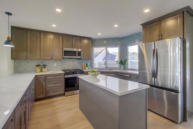 kitchen with pendant lighting, sink, stainless steel appliances, light hardwood / wood-style floors, and light stone countertops