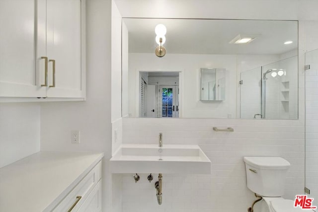 bathroom with toilet, sink, tile walls, a shower with door, and backsplash