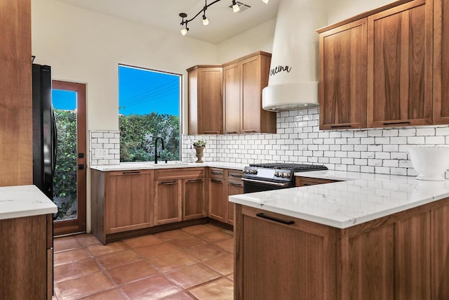 kitchen with range with gas stovetop, decorative backsplash, light stone counters, kitchen peninsula, and custom range hood