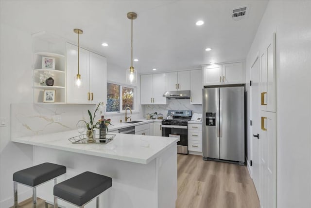 kitchen featuring appliances with stainless steel finishes, light stone counters, white cabinets, decorative light fixtures, and kitchen peninsula