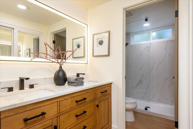 bathroom with hardwood / wood-style flooring, vanity, toilet, and a tile shower