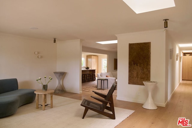 living area with a skylight, ornamental molding, and light hardwood / wood-style floors