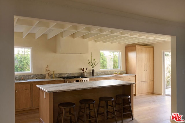 kitchen with range, light wood-type flooring, a kitchen breakfast bar, a kitchen island, and beam ceiling