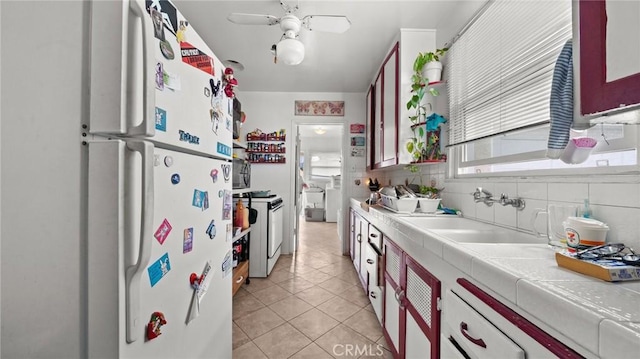 kitchen with sink, white appliances, tile countertops, ceiling fan, and decorative backsplash