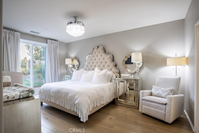 bedroom featuring a notable chandelier, access to exterior, and light hardwood / wood-style flooring