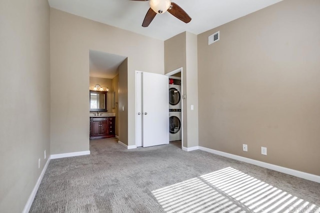 unfurnished bedroom with ensuite bath, light colored carpet, ceiling fan, and stacked washer / dryer