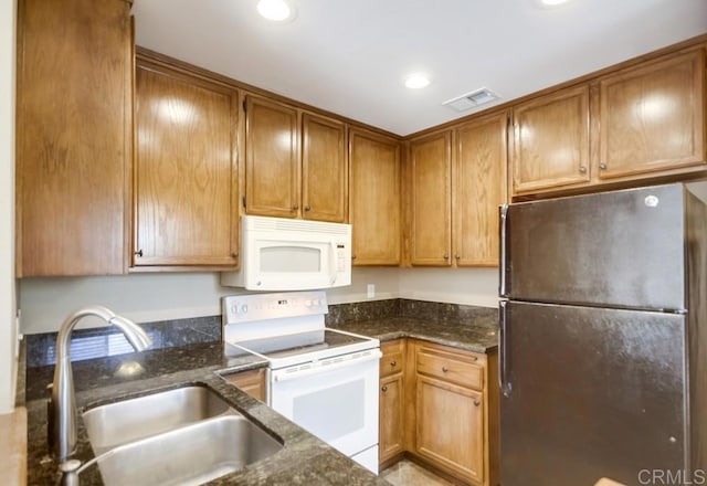 kitchen featuring white appliances, dark stone counters, and sink