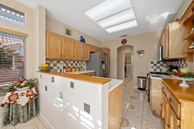 kitchen with light tile patterned flooring, stainless steel appliances, kitchen peninsula, and decorative backsplash