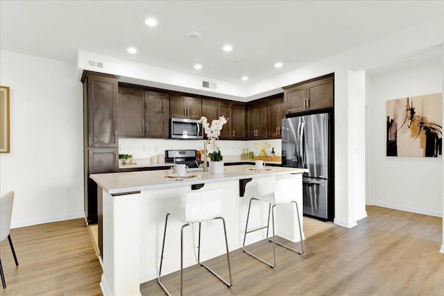 kitchen featuring a kitchen island with sink, dark brown cabinets, stainless steel appliances, and light hardwood / wood-style flooring