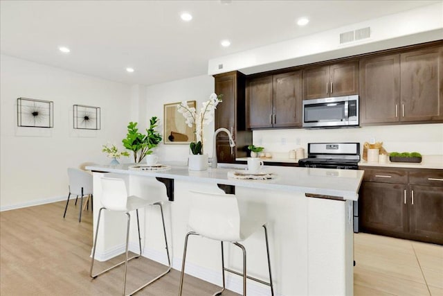 kitchen featuring dark brown cabinetry, appliances with stainless steel finishes, sink, and a kitchen island with sink