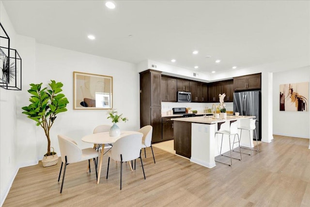 kitchen featuring a kitchen island, appliances with stainless steel finishes, a kitchen bar, dark brown cabinets, and light hardwood / wood-style flooring