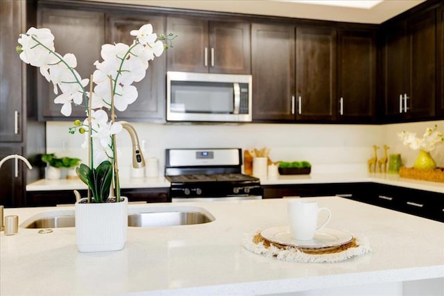 kitchen featuring dark brown cabinetry, light stone countertops, stainless steel appliances, and sink