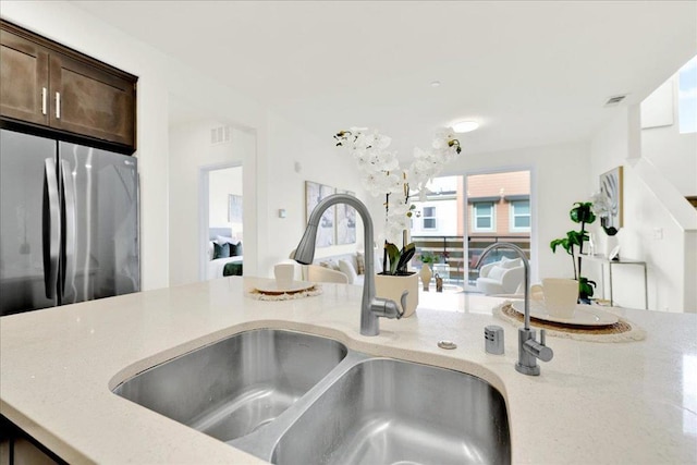 kitchen featuring dark brown cabinetry, sink, stainless steel fridge, and light stone countertops