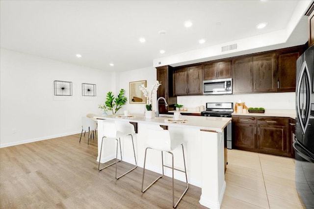 kitchen with sink, a kitchen breakfast bar, an island with sink, stainless steel appliances, and light hardwood / wood-style floors