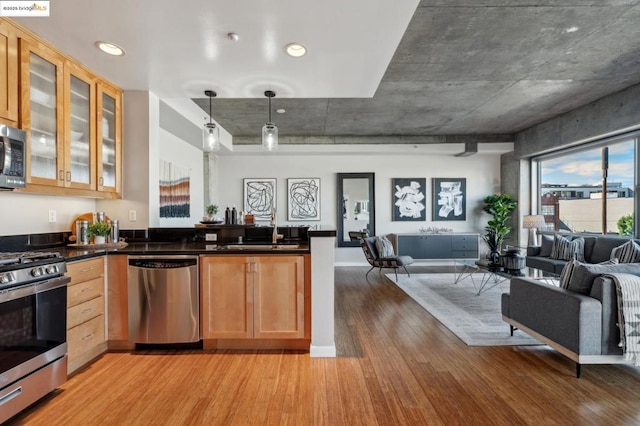 kitchen with light brown cabinetry, sink, light wood-type flooring, pendant lighting, and stainless steel appliances