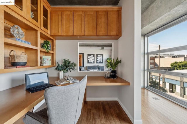 home office with built in desk and dark hardwood / wood-style flooring