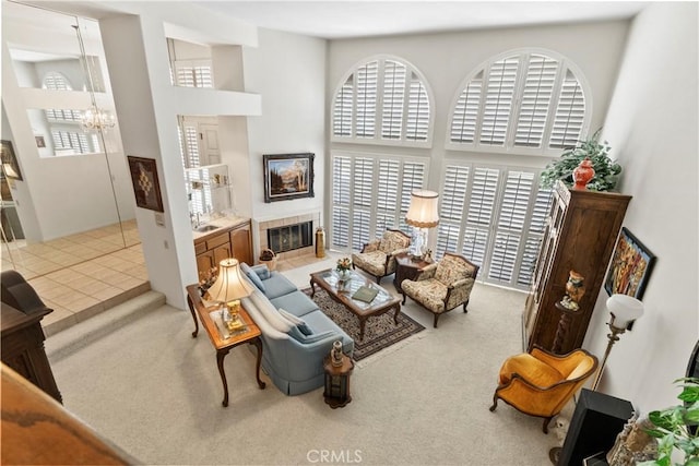 carpeted living room featuring a high ceiling, a tile fireplace, and a notable chandelier