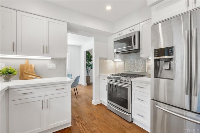 kitchen with hardwood / wood-style flooring, decorative backsplash, white cabinets, and appliances with stainless steel finishes