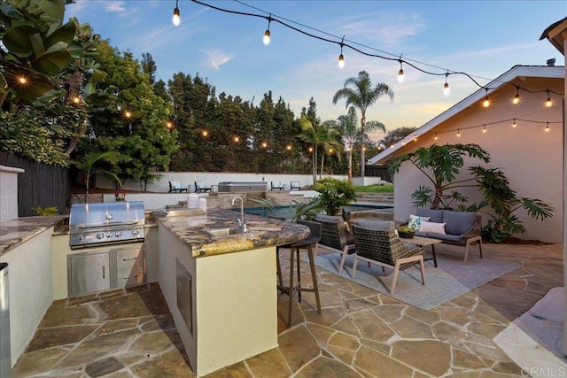 patio terrace at dusk featuring exterior kitchen, area for grilling, and a wet bar