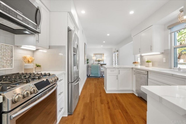 kitchen with sink, white cabinets, kitchen peninsula, stainless steel appliances, and light hardwood / wood-style flooring