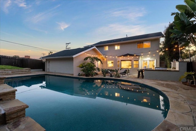 pool at dusk with area for grilling, a patio area, and exterior bar