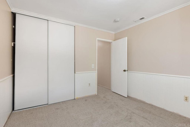 unfurnished bedroom featuring light carpet, ornamental molding, and a closet