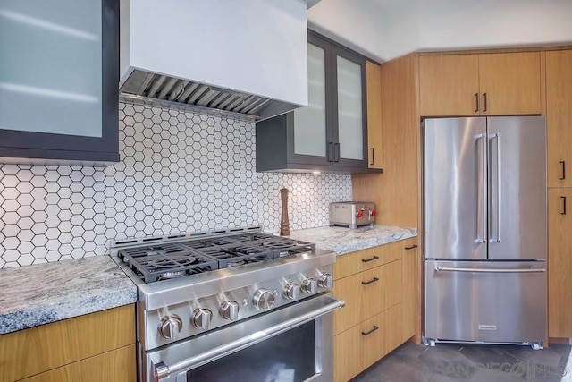 kitchen with light stone counters, decorative backsplash, premium range hood, and appliances with stainless steel finishes