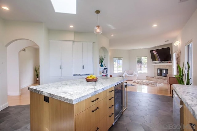 kitchen with wine cooler, a center island, light brown cabinets, stainless steel dishwasher, and pendant lighting