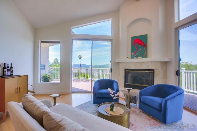 living room featuring a tiled fireplace, high vaulted ceiling, and light hardwood / wood-style floors