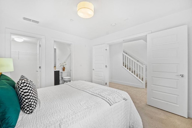 bedroom with a walk in closet, light colored carpet, ensuite bath, and a closet