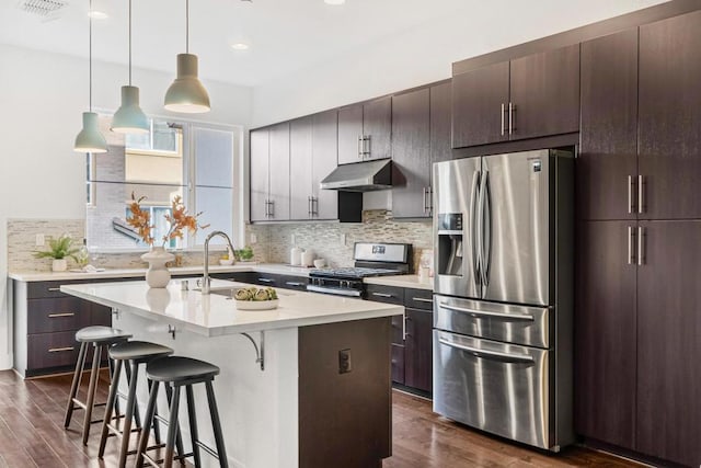 kitchen featuring sink, a kitchen island with sink, stainless steel appliances, dark brown cabinetry, and a kitchen bar