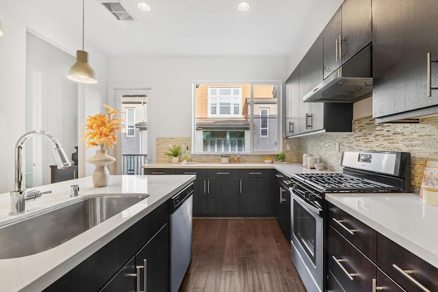 kitchen with appliances with stainless steel finishes, sink, backsplash, hanging light fixtures, and dark wood-type flooring