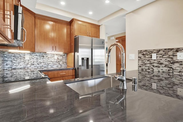 kitchen with decorative backsplash, dark stone countertops, brown cabinets, and appliances with stainless steel finishes