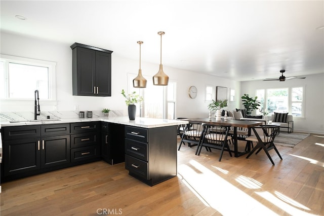 kitchen with hanging light fixtures, sink, light hardwood / wood-style floors, and kitchen peninsula