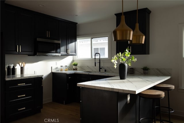 kitchen featuring a breakfast bar, sink, light stone counters, hanging light fixtures, and kitchen peninsula