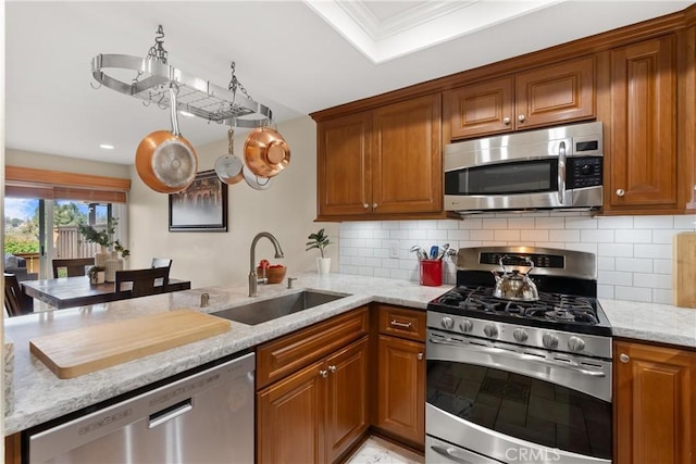 kitchen featuring sink, stainless steel appliances, light stone countertops, decorative backsplash, and kitchen peninsula