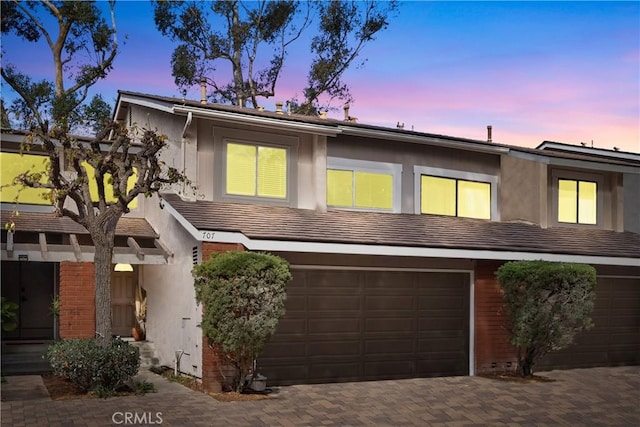 view of property with a garage, decorative driveway, brick siding, and stucco siding