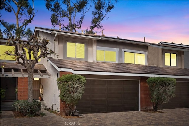 multi unit property with brick siding, decorative driveway, an attached garage, and stucco siding