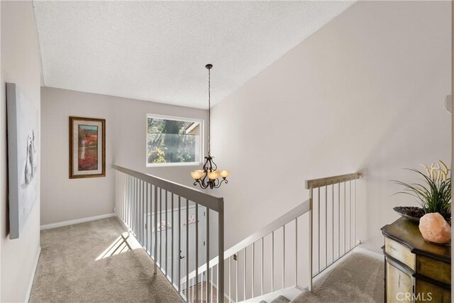 hallway with carpet flooring, a textured ceiling, and an inviting chandelier