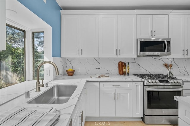 kitchen featuring stainless steel appliances, sink, white cabinets, and light stone counters